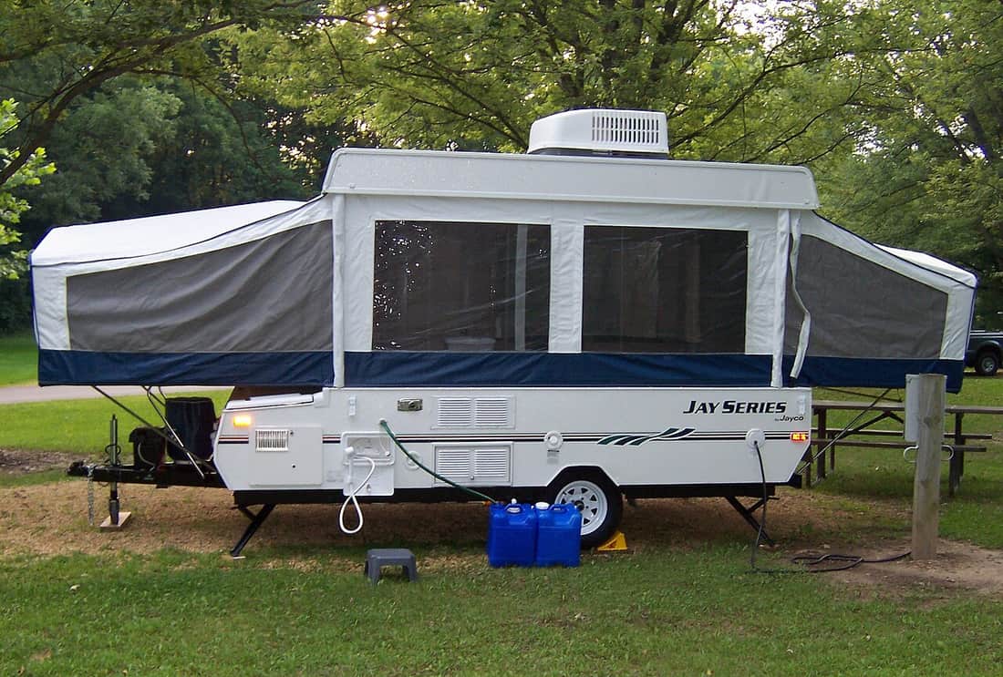 A pop-up camper trailer set up on a lawn, showing the tongue and coupler at the front